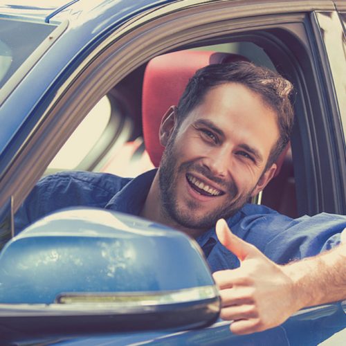 Car side window. Man driver happy smiling showing thumbs up driving sport blue car isolated outside parking lot background. Handsome young man excited about his new vehicle. Positive face expression